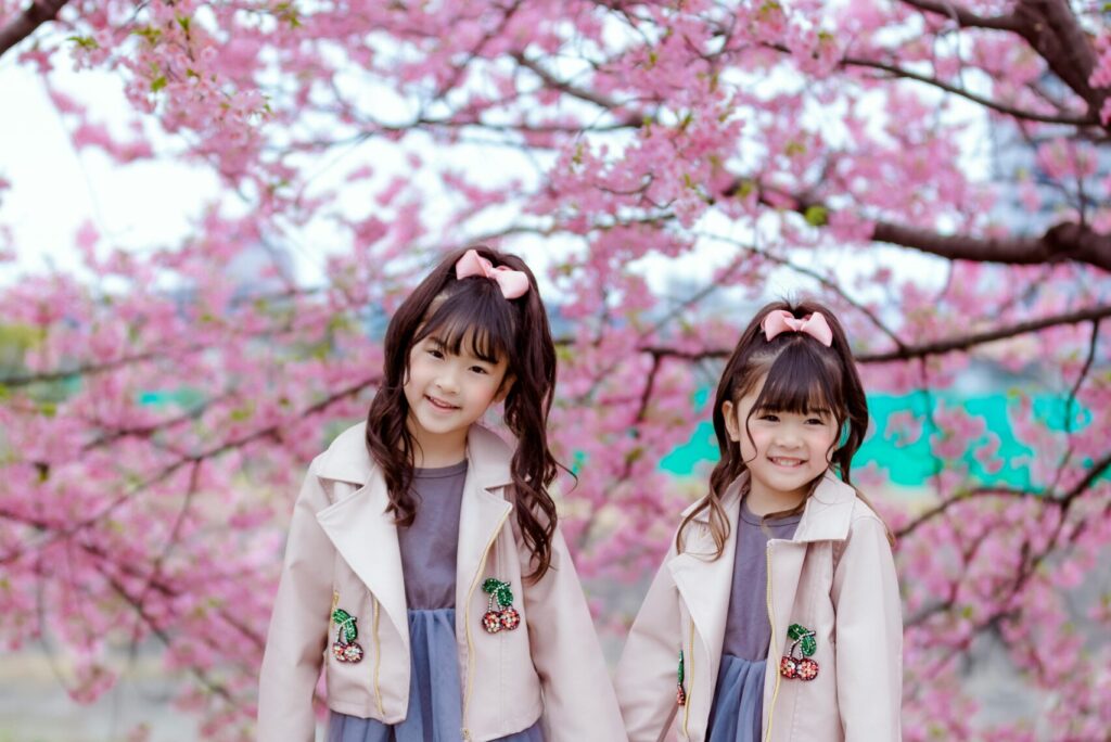 two pretty girls standing under a cherry blossom tree