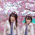 two pretty girls standing under a cherry blossom tree